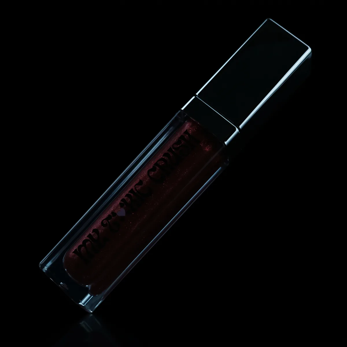 The gloss lying closed on a black surface, almost invisible in the dark